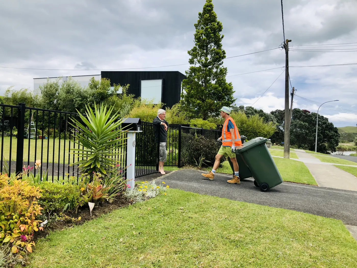 a man pushing a trash can next to a fence