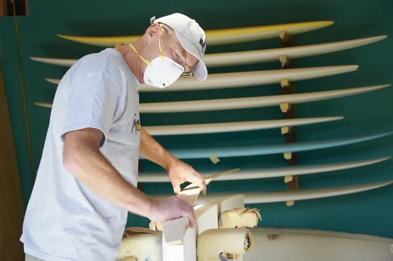 a man wearing a mask and working on a surfboard